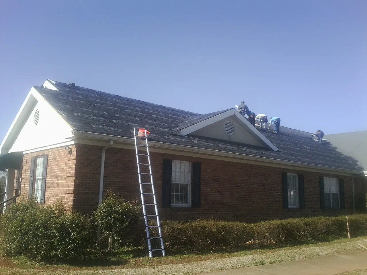 Crew tearing shingles off a brick ranch roof with a ladder set — Emergency Roof Repair work by our crew in Smithfield